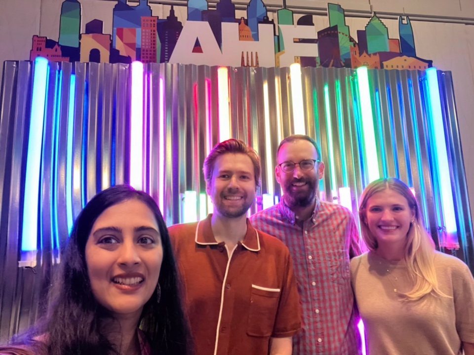 Four members of the Banquet team in front of the AHF conference sign